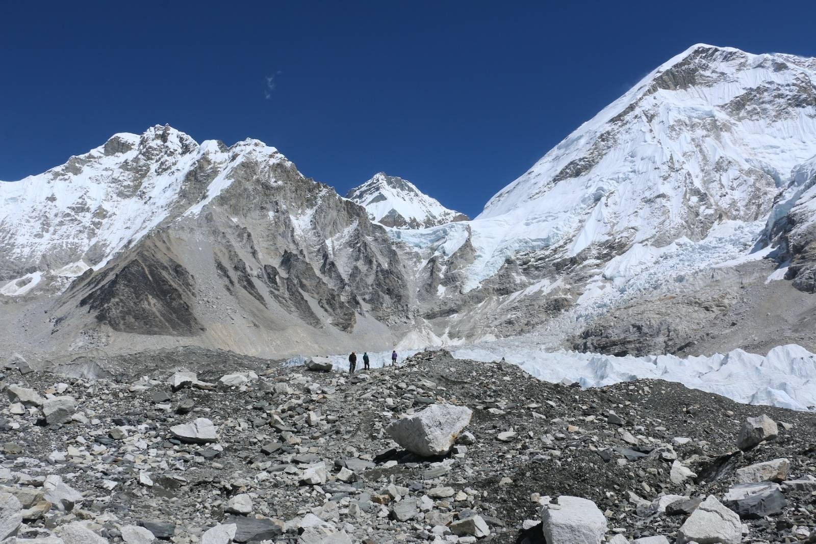 Trekkers ascending a Himalayan trail toward base camp viewpoint with snow-capped mountains, glaciers, and rugged alpine terrain in the background of Nepal.