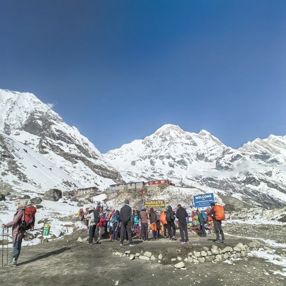 Group of trekkers standing together at Annapurna Base Camp, surrounded by snowy peaks and the natural Himalayan amphitheater.