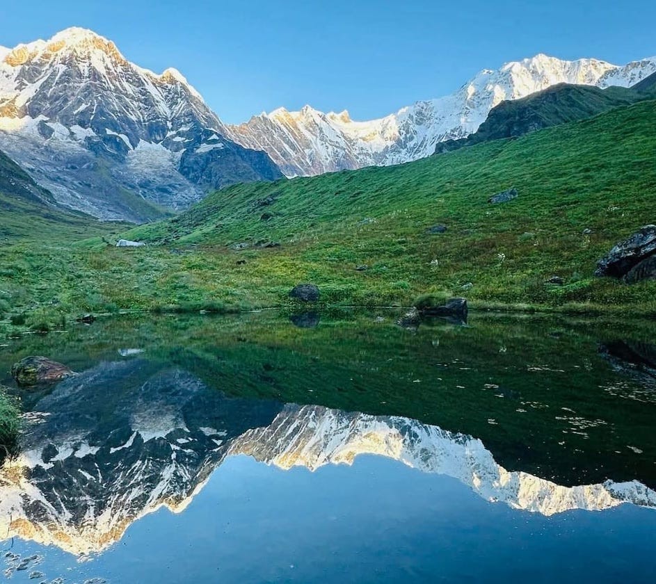 Annapurna Base Camp in September with lush green meadows, snow-covered Annapurna peaks, and a crystal-clear alpine pond reflecting the Himalayan landscape.