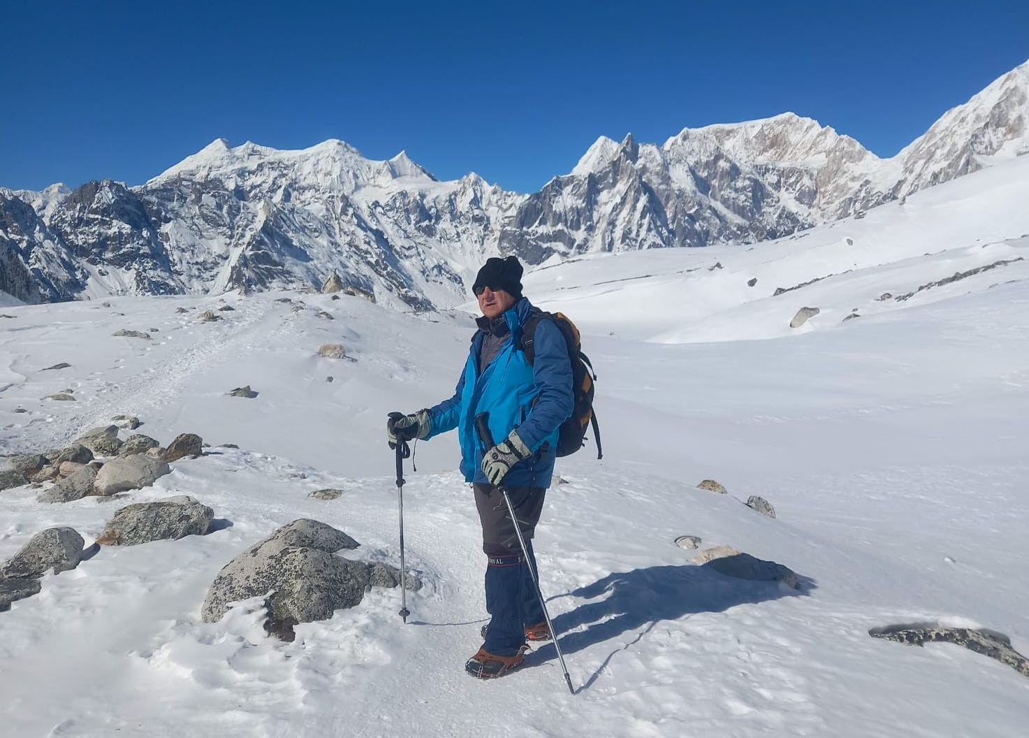 Trekker on the Manaslu Circuit wearing a warm beanie, neck gaiter, insulated gloves, sunglasses, and layered clothing for protection against cold winds and freezing November temperatures.