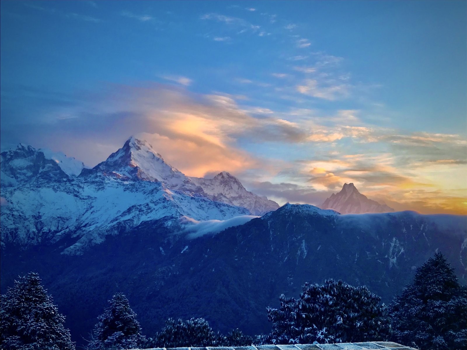 The first golden rays of sunrise light up the massive, glowing snow-capped peaks of the Dhaulagiri and Annapurna mountain ranges against a deep orange and purple gradient sky.