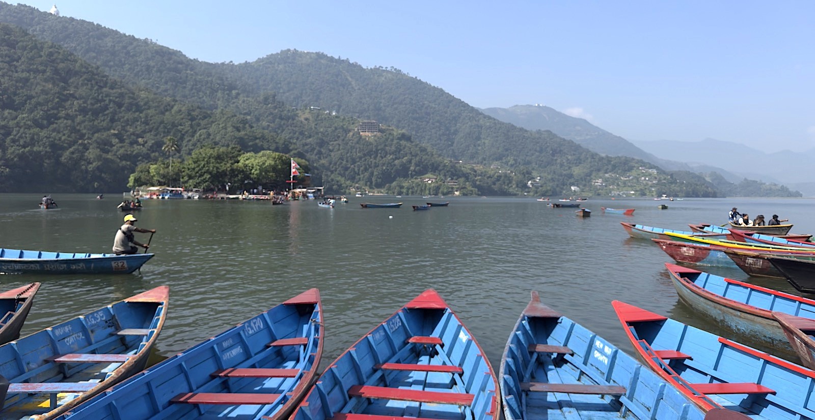 Colorful boats floating on Phewa Lake with reflections of the Annapurna Himalayas and Pokhara city in Nepal.