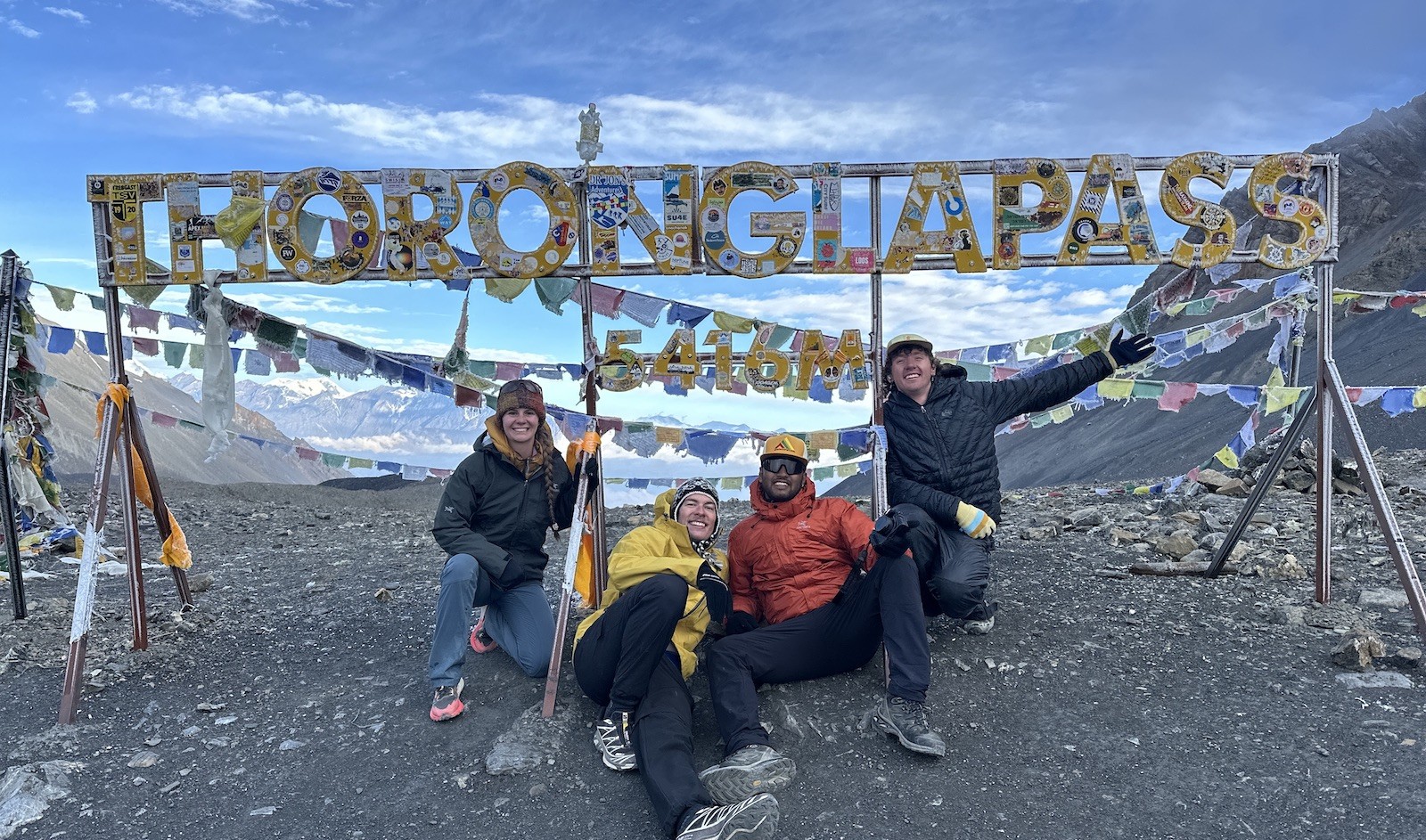 Trekkers crossing Thorong La Pass surrounded by snow-covered Himalayan terrain, prayer flags, and high-altitude mountain scenery in Nepal.