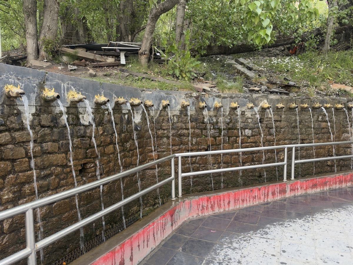 The 108 sacred water spouts (Muktidhara) at Muktinath Temple, with pilgrims bathing beneath the stone taps surrounded by prayer flags and the stunning Himalayan landscape in Mustang, Nepal.