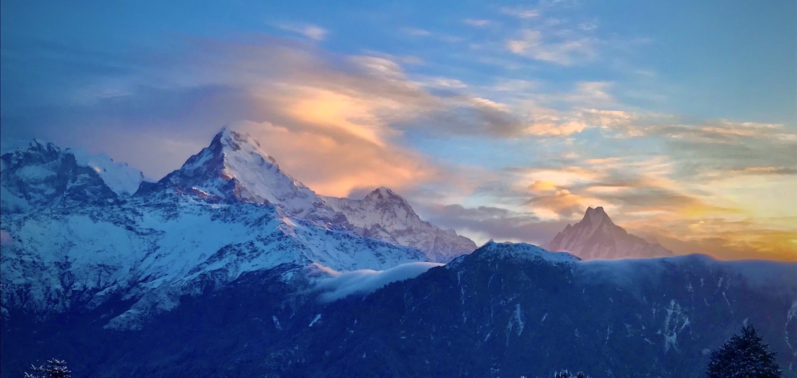 Winter landscape at Poon Hill with snow-covered Annapurna South and Machhapuchhre (Fishtail) glowing at sunrise beneath colorful clouds in Nepal's Annapurna region."