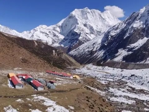 Trekking lodge at Dharamsala (Larke Phedi) surrounded by rocky high-altitude terrain and snow-covered Himalayan mountains.