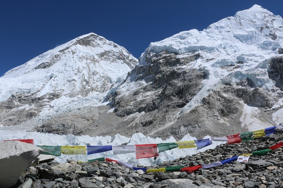 Everest Base Camp under clear blue skies in December with the Khumbu Glacier, colorful prayer flags, and snow-covered Himalayan peaks