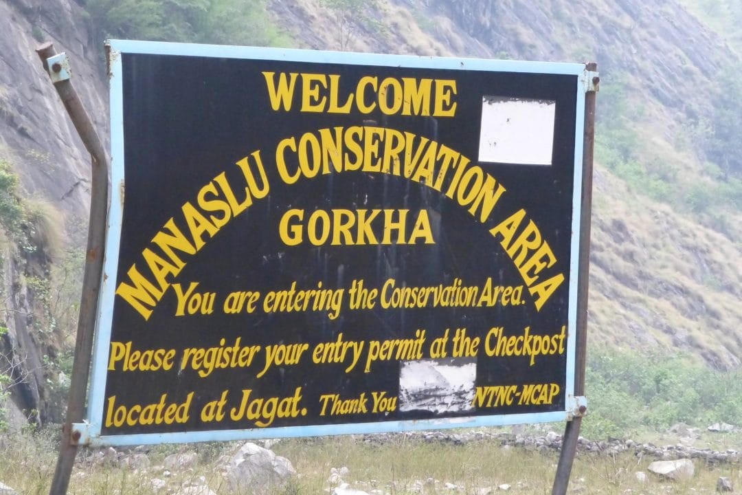 Manaslu Conservation Area entrance signboard along the trekking trail in Nepal, with surrounding forests, mountain scenery, and information welcoming visitors to the protected Himalayan region.