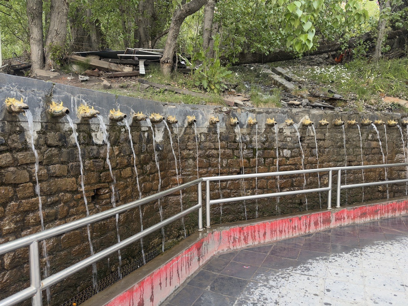 The 108 sacred water spouts (Muktidhara) at Muktinath Temple, with pilgrims bathing beneath the stone taps surrounded by prayer flags and the stunning Himalayan landscape in Mustang, Nepal.