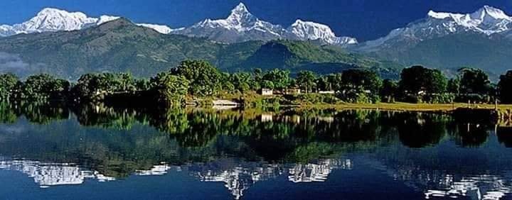 Snow-capped Himalayan mountains reflected on the calm waters of Phewa Lake in Pokhara, Nepal.