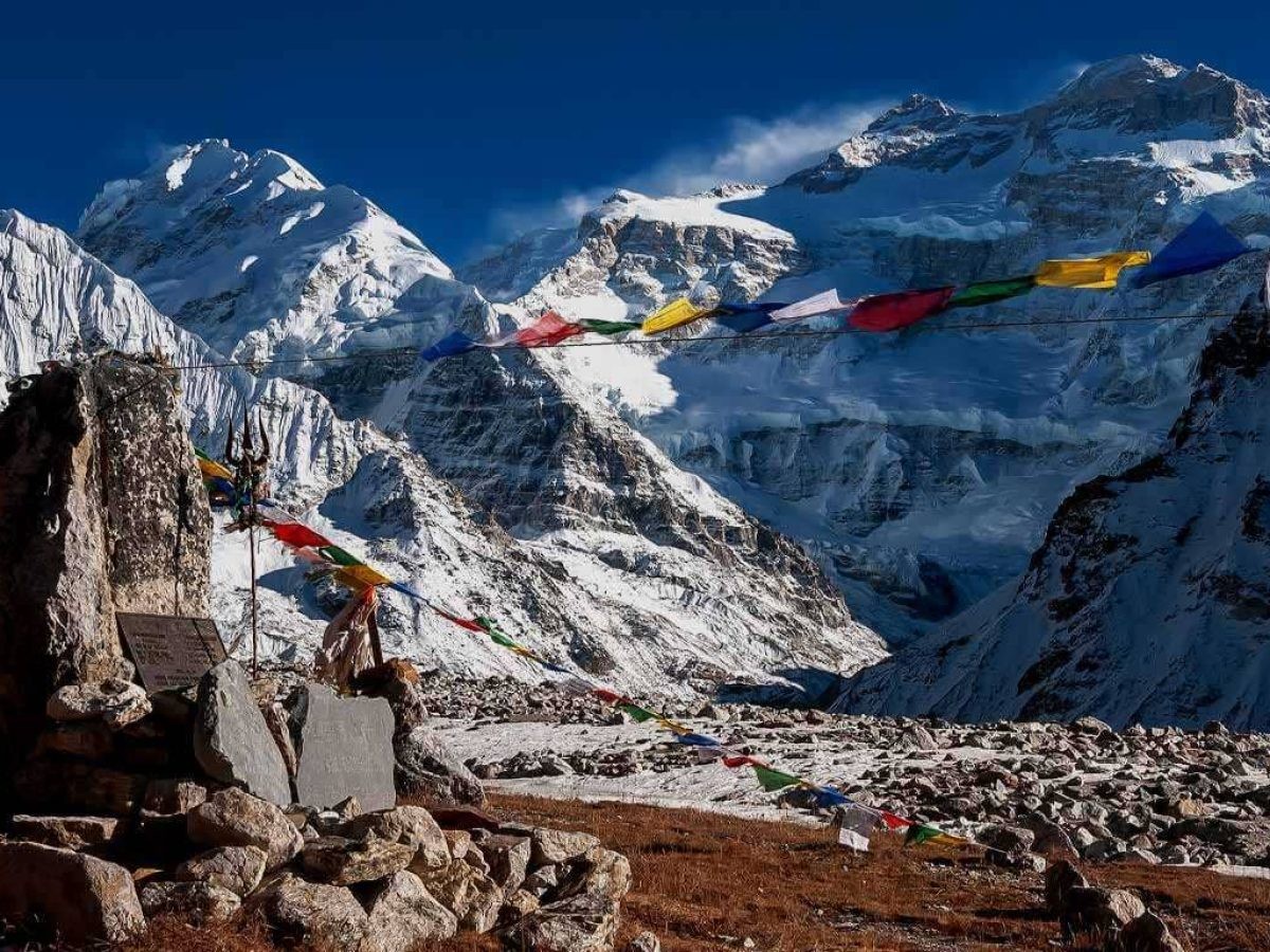 Kanchenjunga North Base Camp (Pangpema) surrounded by towering snow-covered Himalayan peaks, glaciers, rocky moraine, and colourful prayer flags beneath the majestic Mount Kanchenjunga