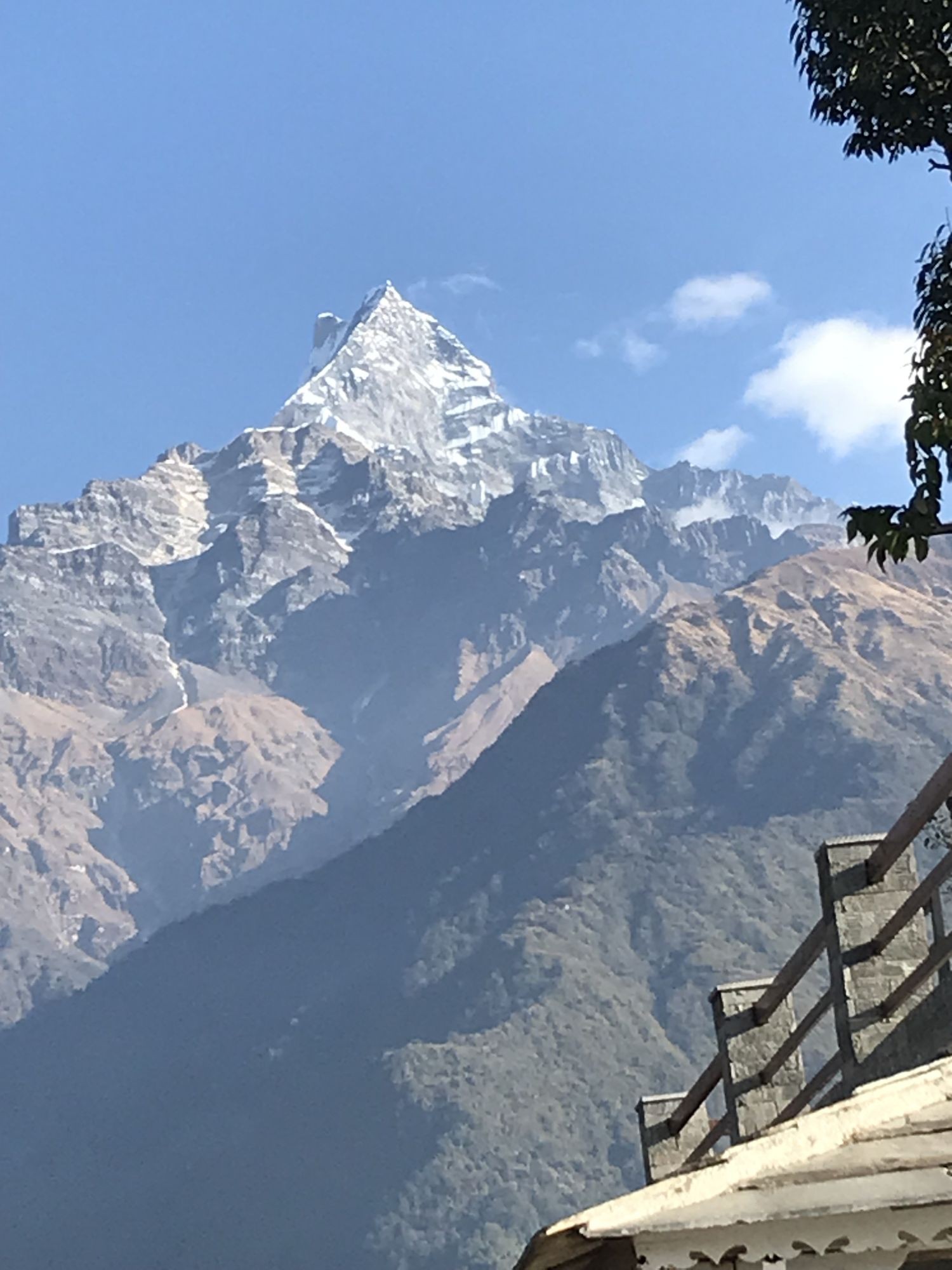 View of Machapuchare (Fishtail Mountain) seen from Sidding Village, with its iconic snow-covered peak rising above green hills and terraced farmland in the Annapurna region of Nepal.