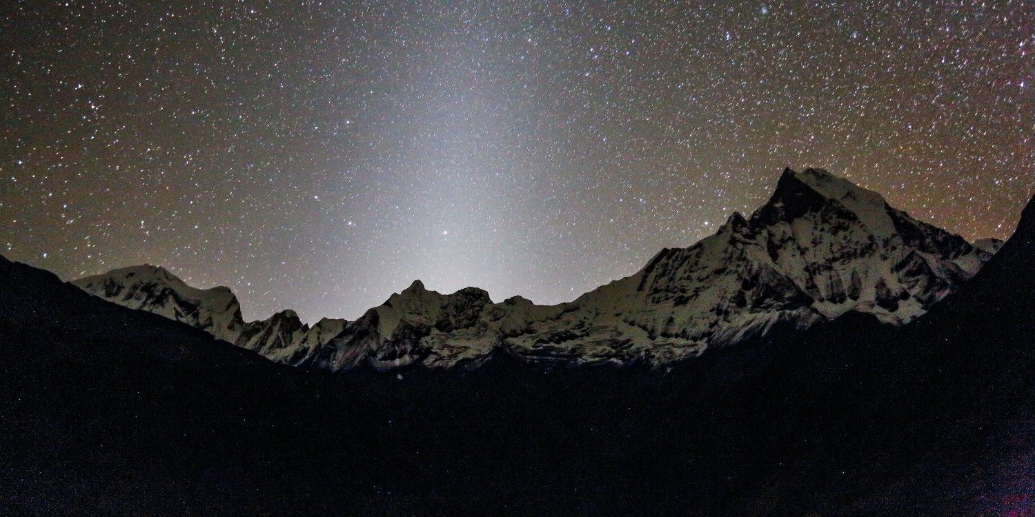 Night view of Annapurna Base Camp beneath a star-filled sky, with the Milky Way shining above snow-covered Himalayan peaks, mountain lodges, and the peaceful Annapurna Sanctuary.
