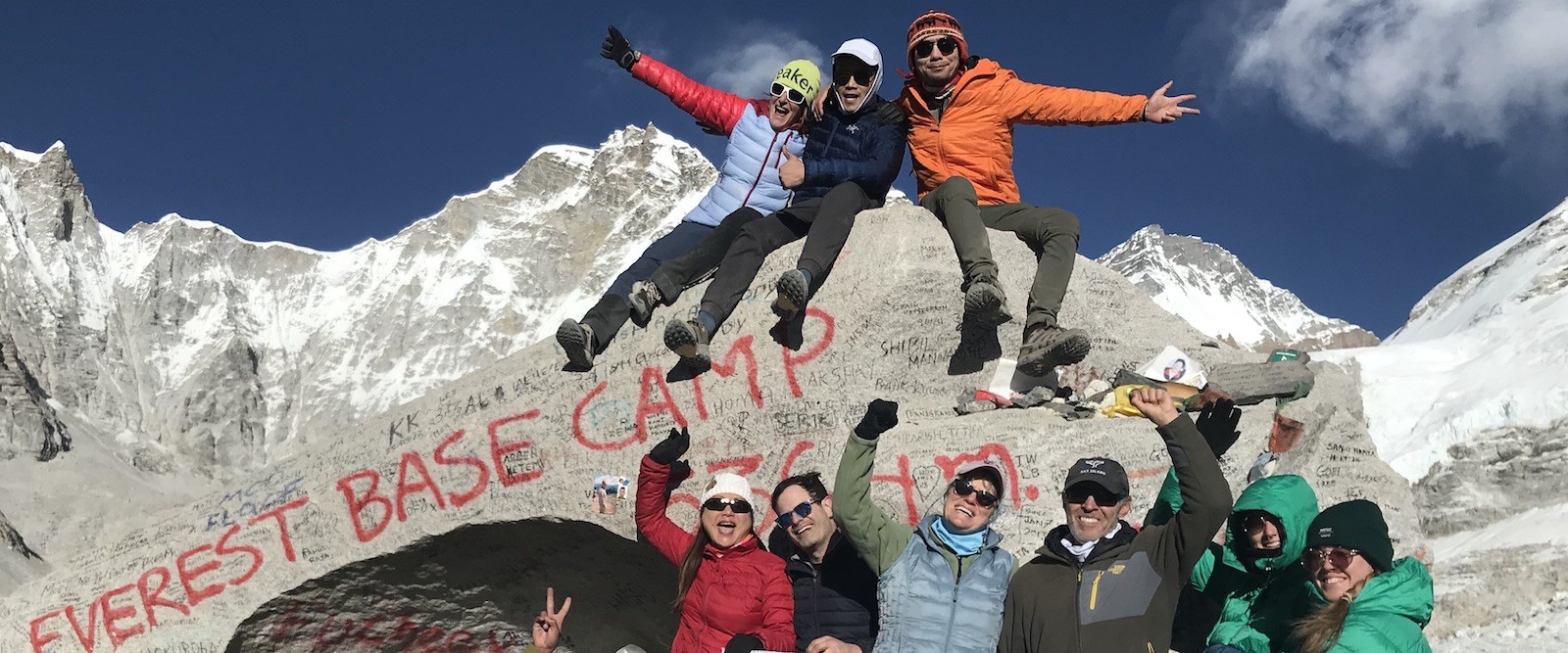 Everest Base Camp trekkers celebrating their successful trek in late November with snow-covered Himalayan peaks in the background.