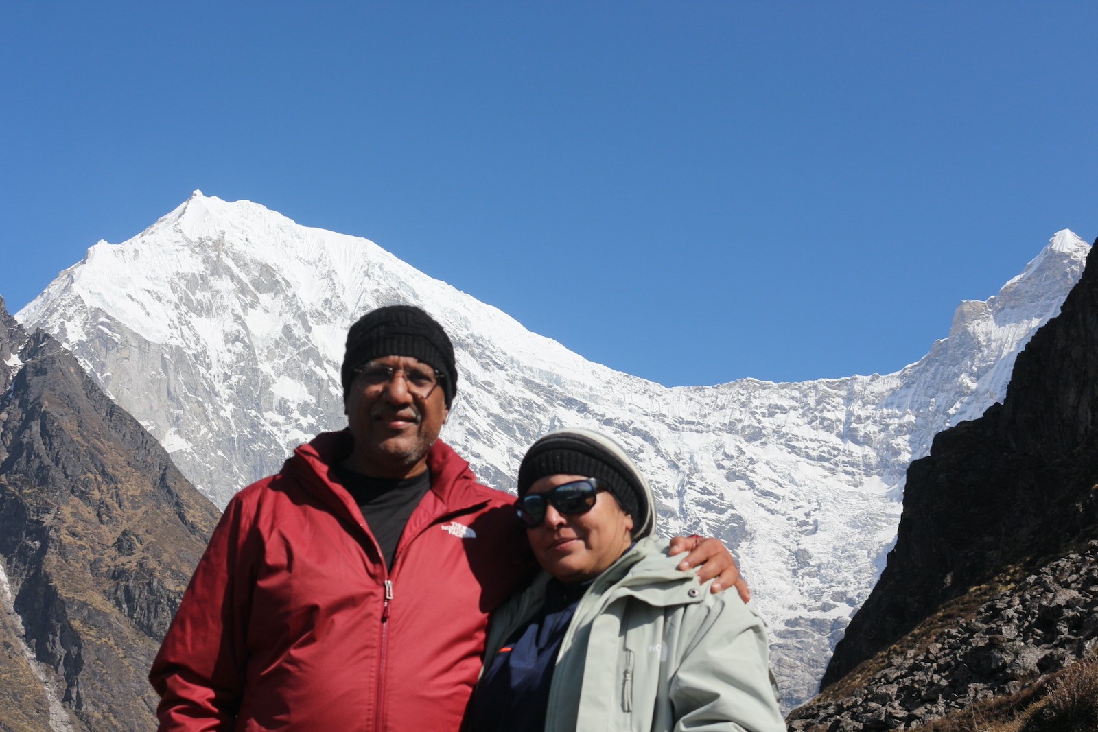 Trekker wearing a down jacket at Kyanjin Gompa surrounded by snow-capped peaks and alpine landscapes in Langtang Valley, Nepal.
