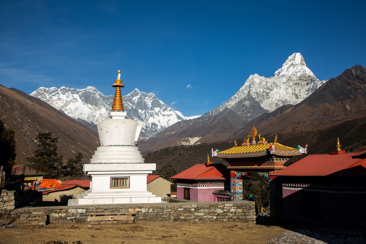 "Tengboche Monastery with a white Buddhist stupa and colorful monastery gate set against the majestic Ama Dablam and snow-capped Himalayan peaks on the Everest Base Camp Trek in Nepal."  