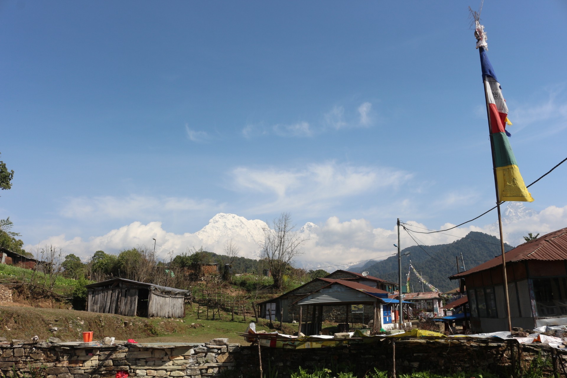 Scenic view of Pothana featuring traditional mountain lodges, forested hills, and panoramic views of the Annapurna Himalayan range along the Mardi Himal trekking route.