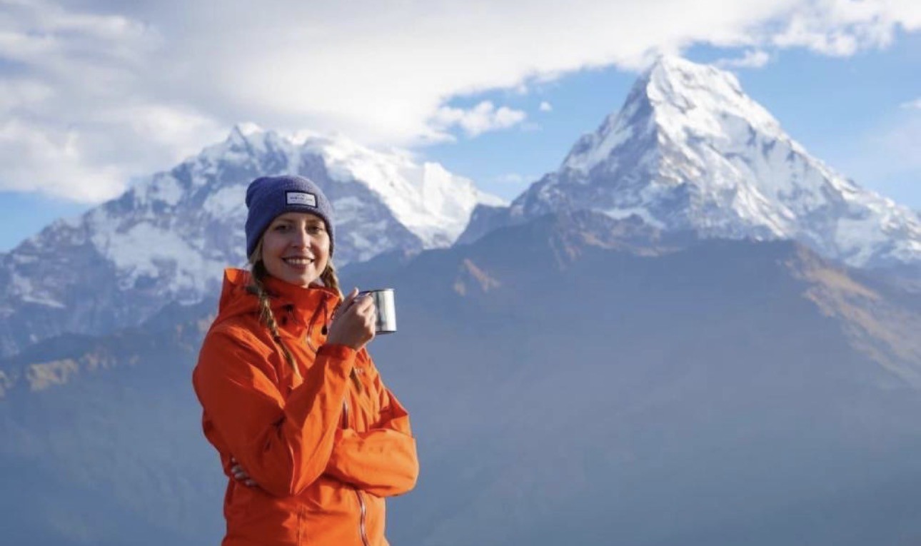 Trekker enjoying a hot cup of tea at Poon Hill Viewpoint during sunrise with the Annapurna and Dhaulagiri mountain ranges in the background.