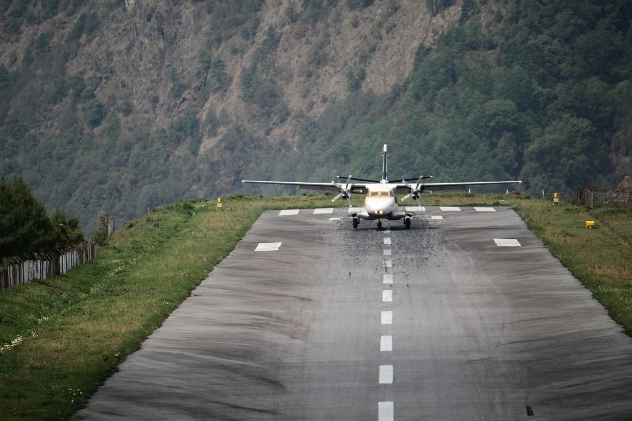 "Lukla Airport with a small Twin Otter aircraft on the runway surrounded by dramatic Himalayan mountains in Nepal, the gateway to the Everest Base Camp Trek."