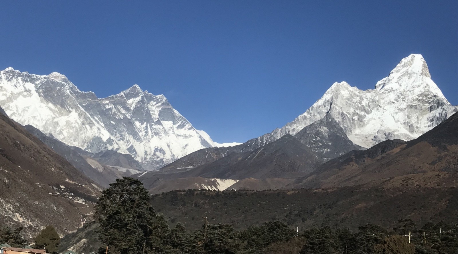 Panoramic view of Mount Everest, Lhotse, Nuptse, and Ama Dablam under a crystal-clear blue sky, with alpine forests and rugged Himalayan valleys on the Everest Base Camp Trek.