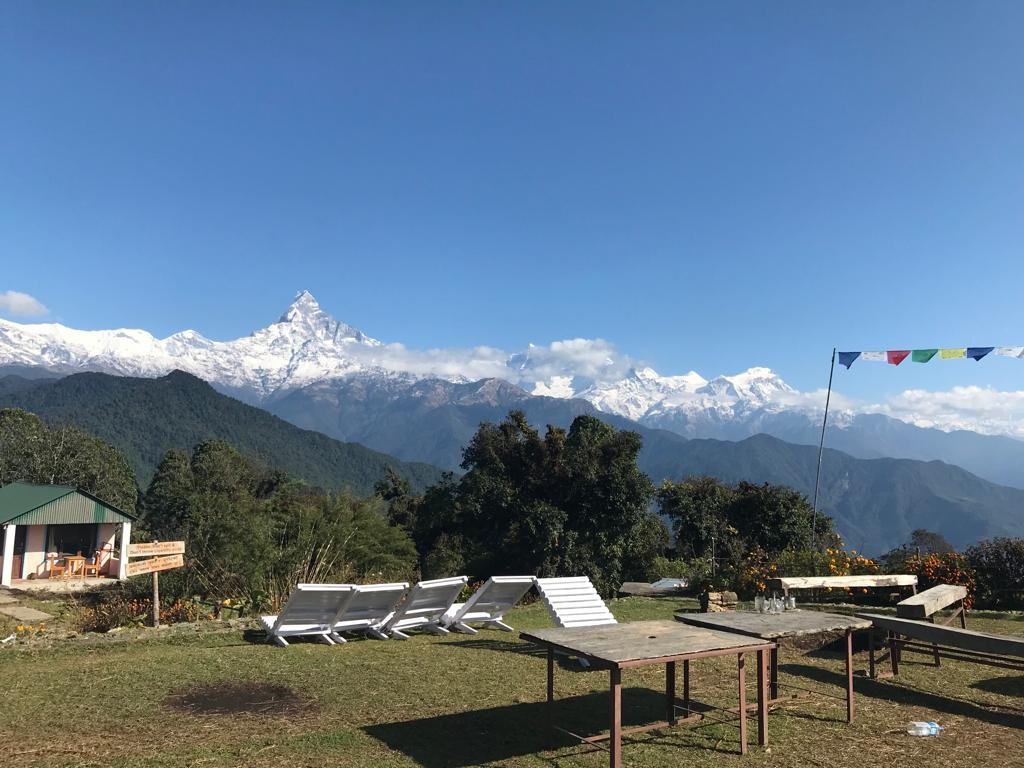 Panoramic view from Australian Camp on the way to the Mardi Himal Trek, featuring Machhapuchhre (Fishtail), the Annapurna mountain range, cozy mountain lodges, green hills, and clear blue autumn skies in Nepal.  