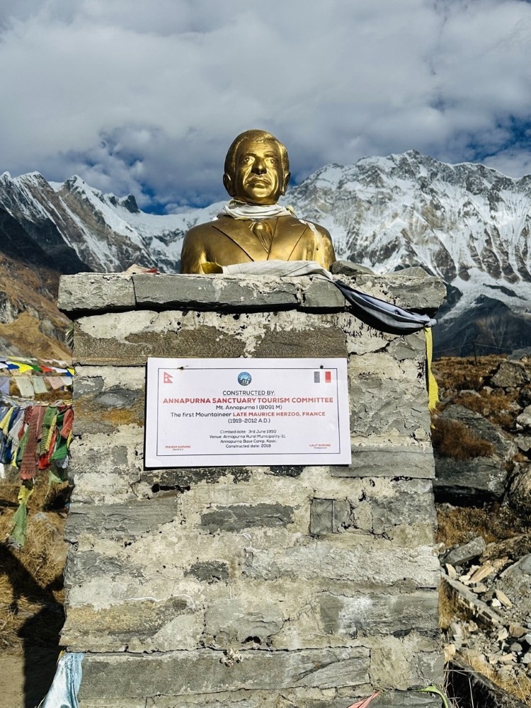 Statue of Maurice Herzog on the Annapurna Base Camp Trek, commemorating the first successful ascent of Annapurna I in 1950, with Himalayan peaks in the background.