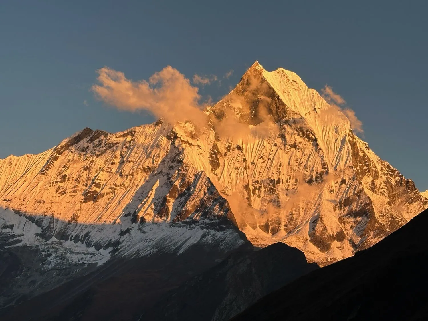 Golden sunlight illuminating Machhapuchhre (Fishtail Mountain), casting warm orange and golden hues across its snow-covered summit and dramatic Himalayan ridges.
