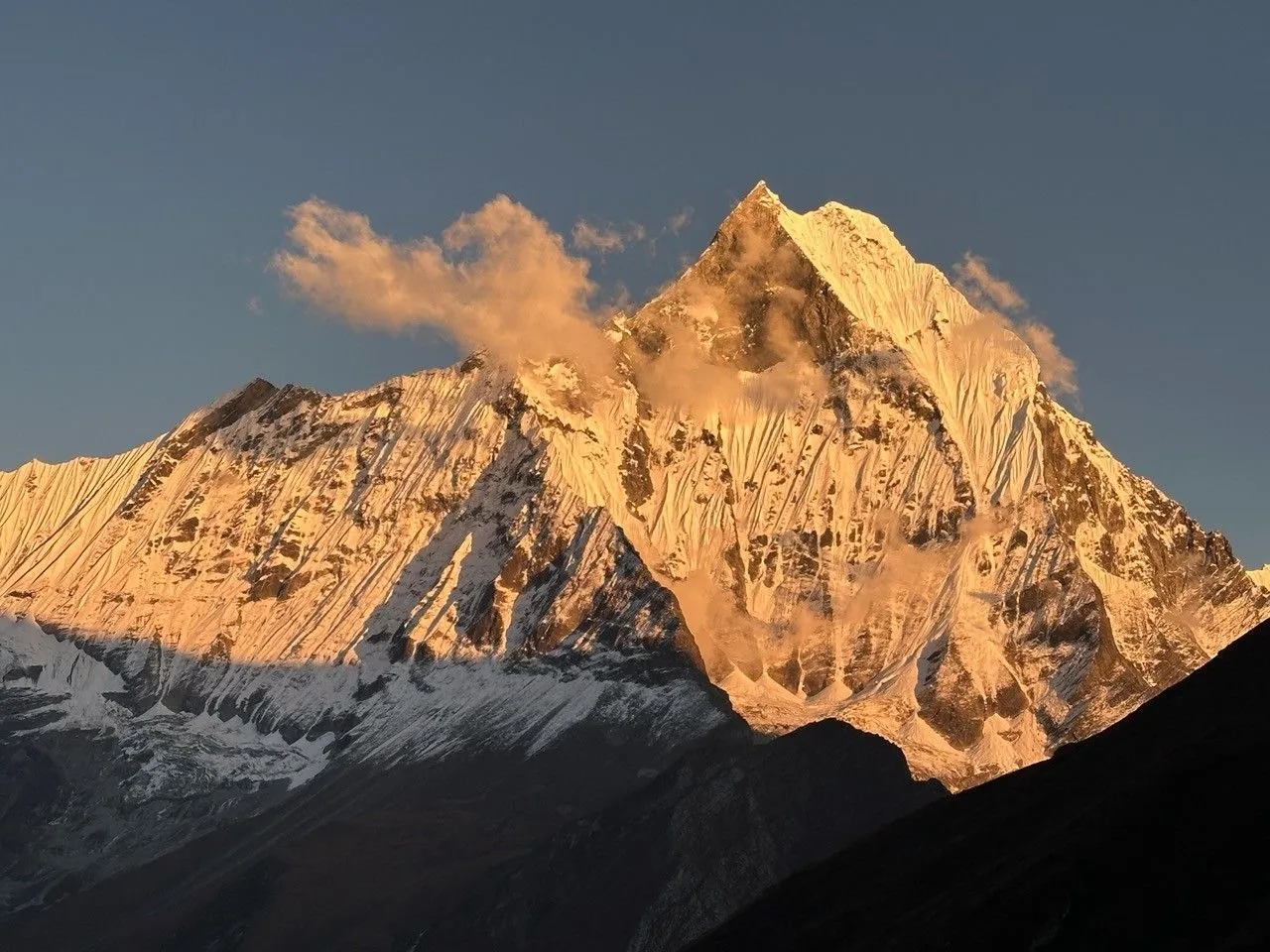 Golden sunlight illuminating the snow-capped peak of Machapuchare (Fishtail Mountain) above the Annapurna region in Nepal.