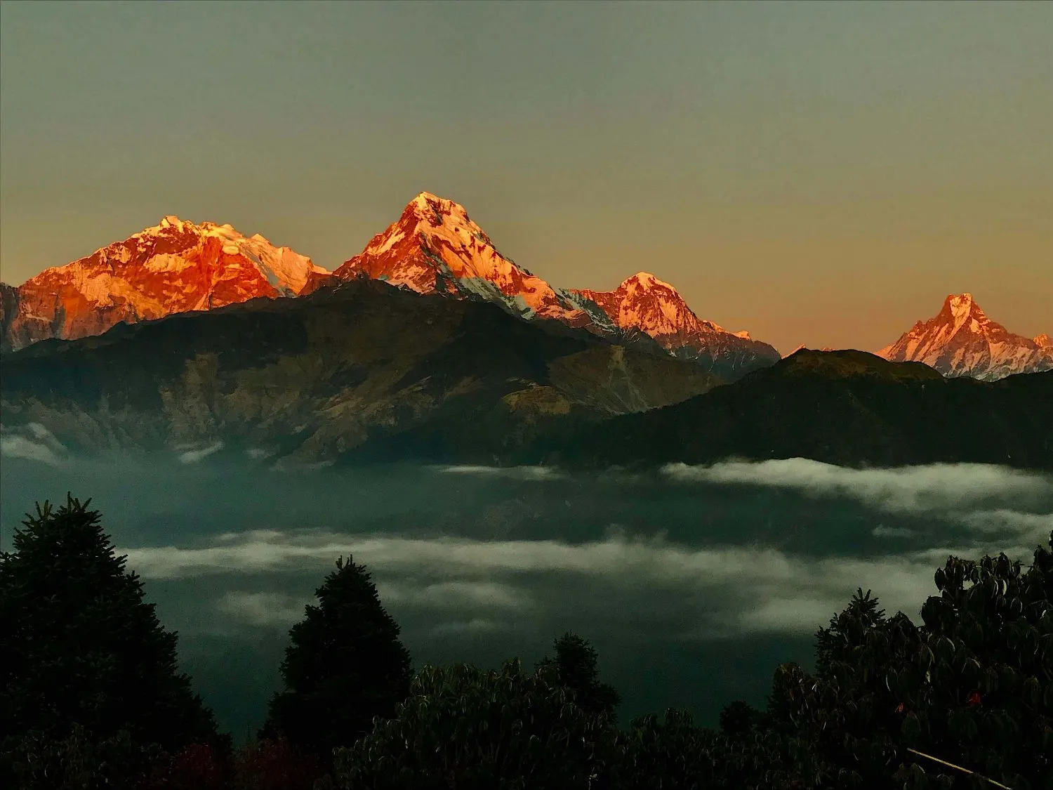 Sunrise view from Poon Hill with golden light illuminating the Annapurna and Dhaulagiri Himalayan ranges above layers of mountain ridges and valleys.