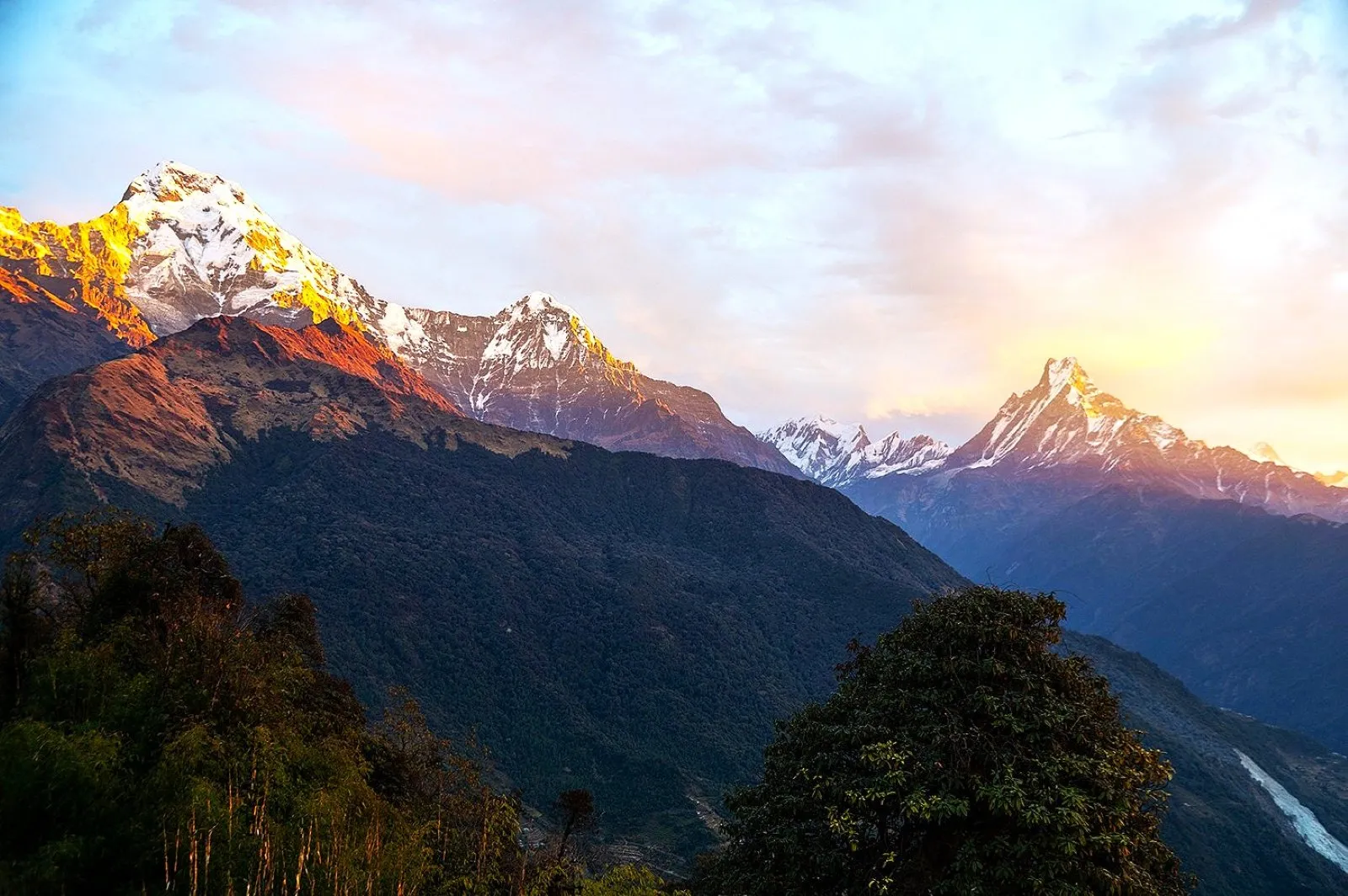 Golden sunrise rays illuminating Annapurna South and Machhapuchhre Fishtail mountains in Nepal.