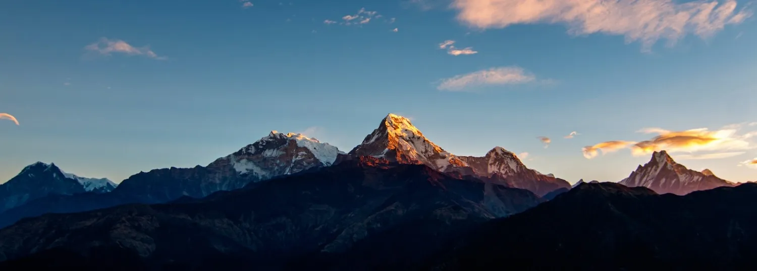 Golden sunrise from Poon Hill illuminating the Annapurna and Dhaulagiri ranges, with warm orange light spreading across snow-capped Himalayan peaks beneath a colorful morning sky.