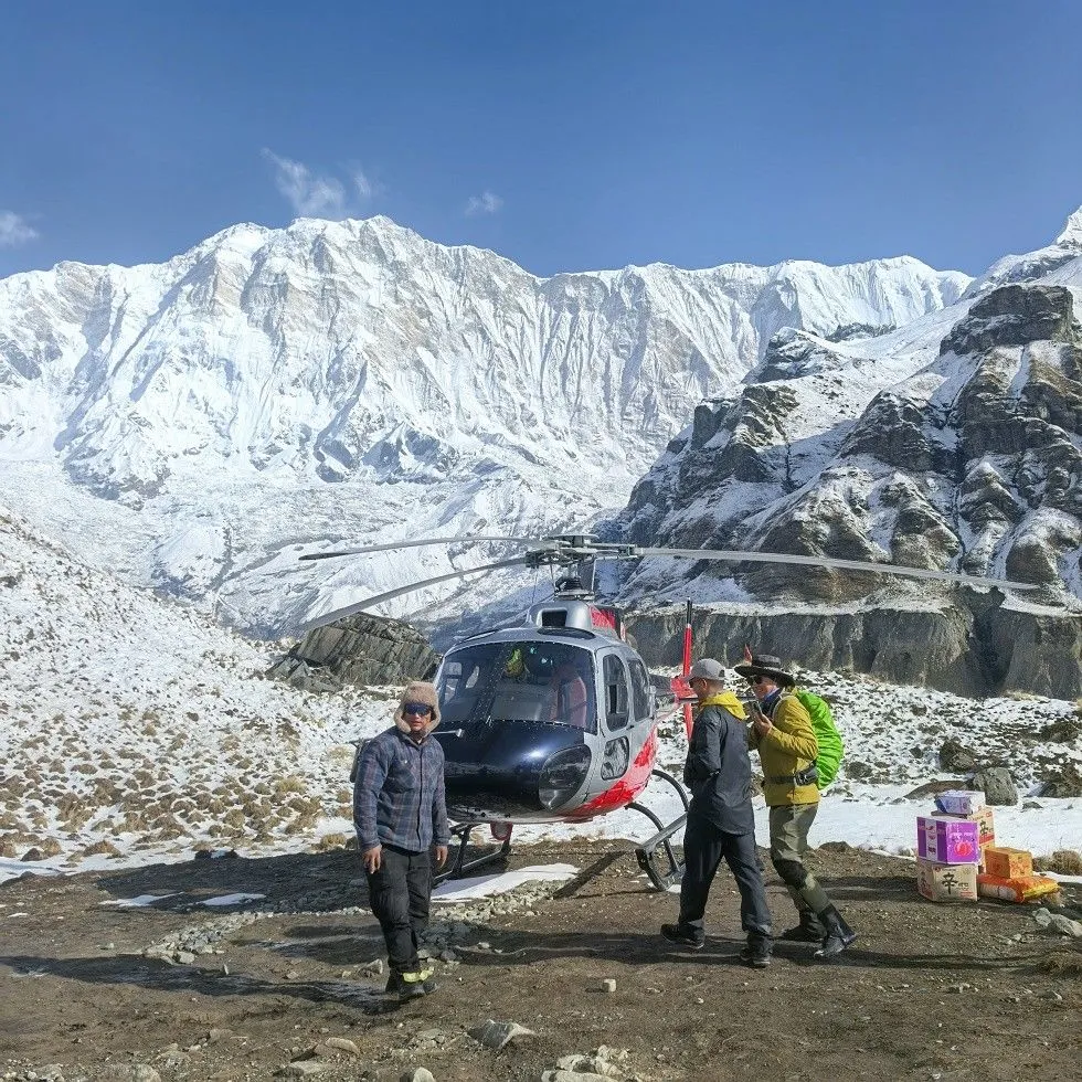 helicopter taking off from Annapurna Base Camp, soaring above the Annapurna Sanctuary with panoramic views of Annapurna I, Machhapuchhre (Fishtail Mountain), glaciers, and snow-covered Himalayan peaks