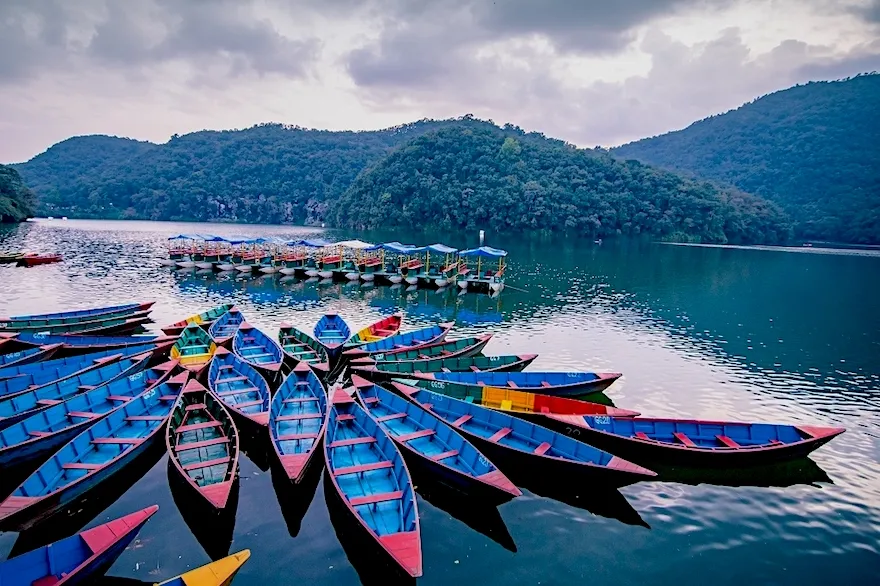 Colorful boats on Phewa Lake in Pokhara with scenic hills and Himalayan views in Nepal.