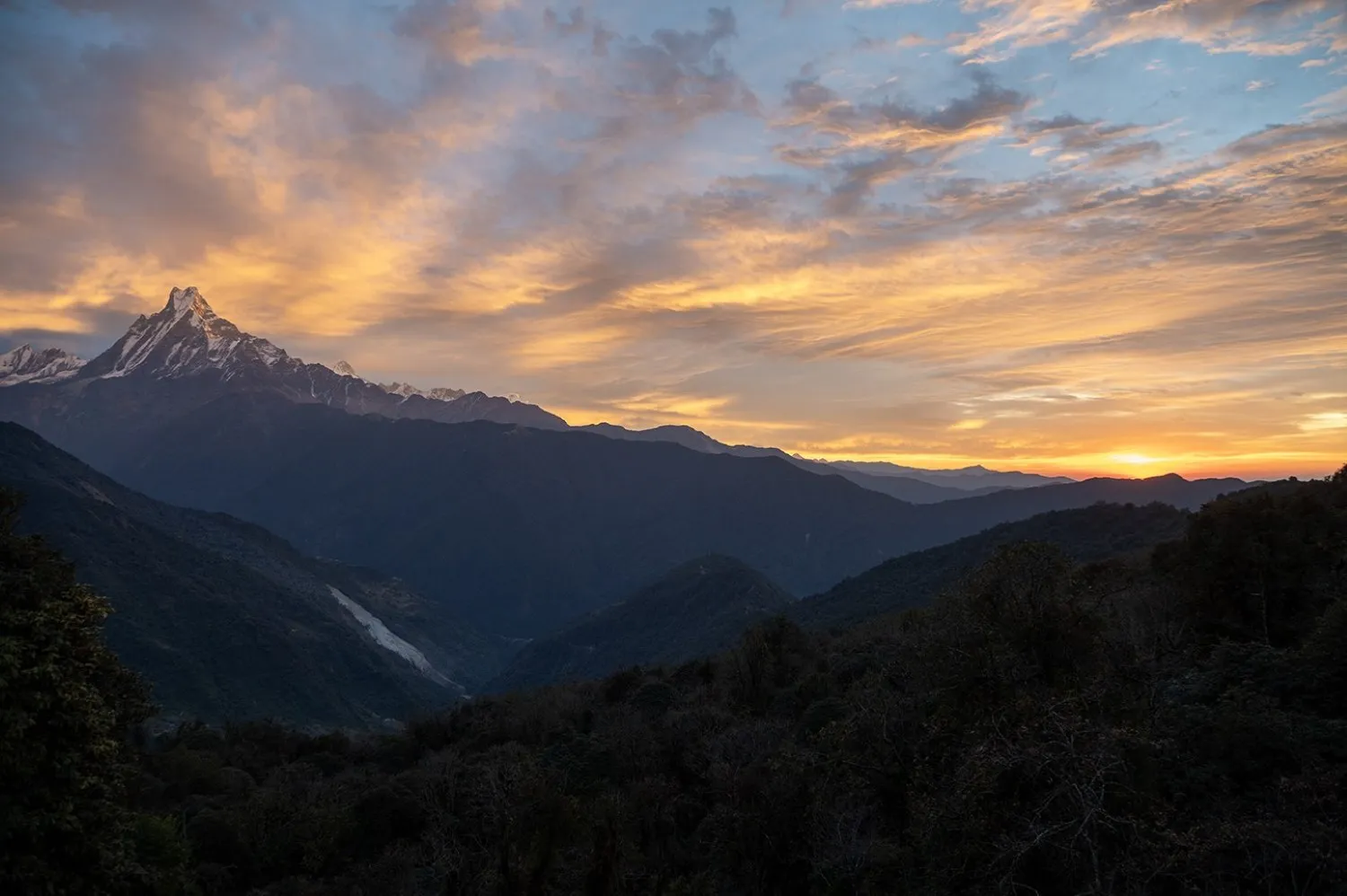 Sunrise view from Tadapani with soft orange clouds glowing in the morning sky, while the iconic Machhapuchhre (Fishtail Mountain) stands majestically above the Himalayan landscape