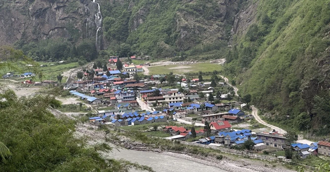 Scenic view of Tal along the Annapurna Circuit Trek, featuring traditional stone houses, waterfalls, a wide river valley, and surrounding Himalayan cliffs.