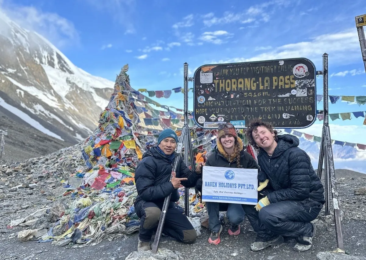 High-altitude trekking scene at Thorong La Pass with prayer flags, and trekkers crossing the highest point of the Annapurna Circuit in Nepal.
