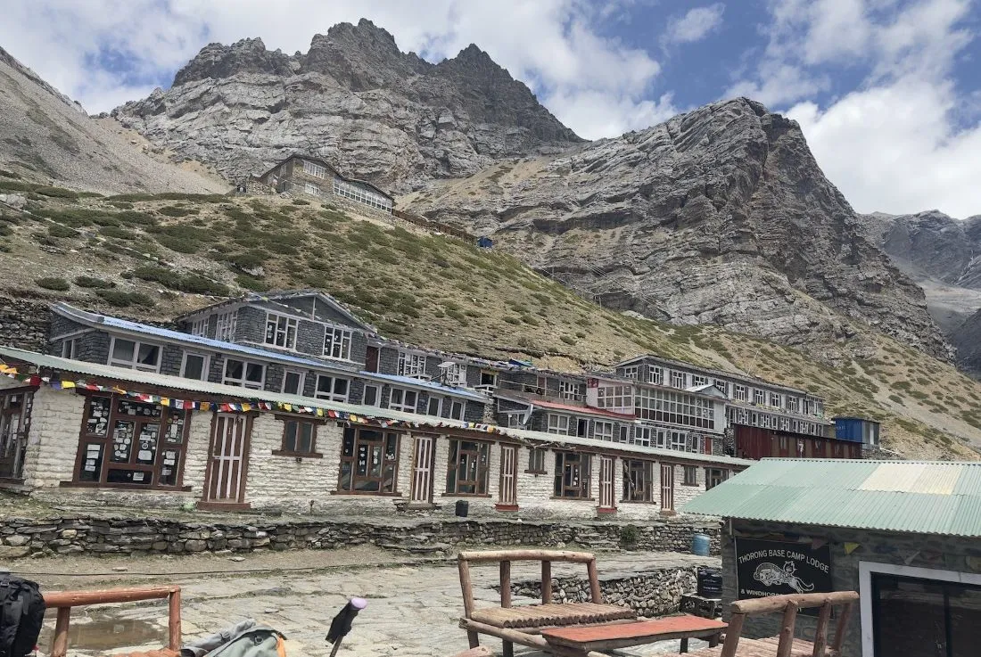High-altitude teahouse settlement at Thorong Phedi surrounded by rugged rocky slopes, snow-dusted Himalayan terrain, and trekking trails leading toward Thorong La Pass.