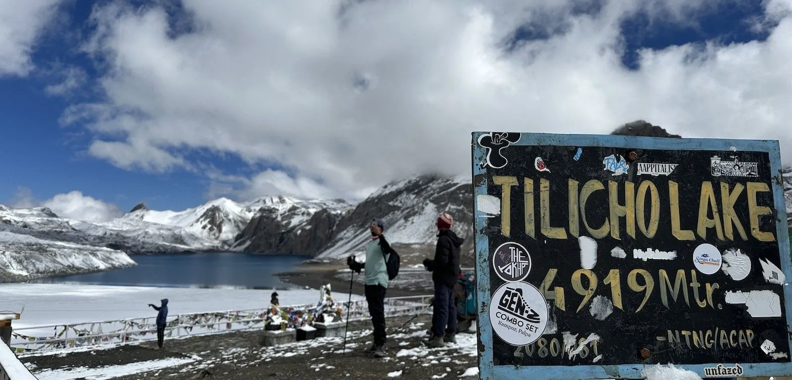 Tilicho Lake with one-third clear turquoise water and two-thirds ice, surrounded by snow-covered Himalayan peaks in Nepal.