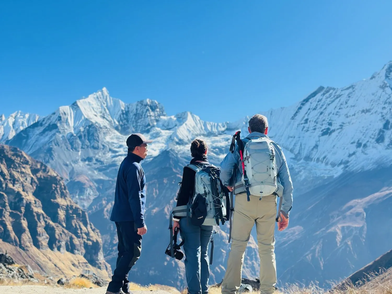 Trekker standing at Annapurna Base Camp on a bright sunny day under a crystal-clear blue sky, admiring the breathtaking snow-capped Annapurna peaks and the spectacular Himalayan landscape.