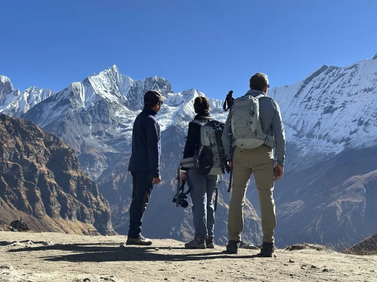Trekker standing on a mountain trail looking at stunning snow-capped Himalayan peaks with clear skies and dramatic alpine scenery in Nepal.